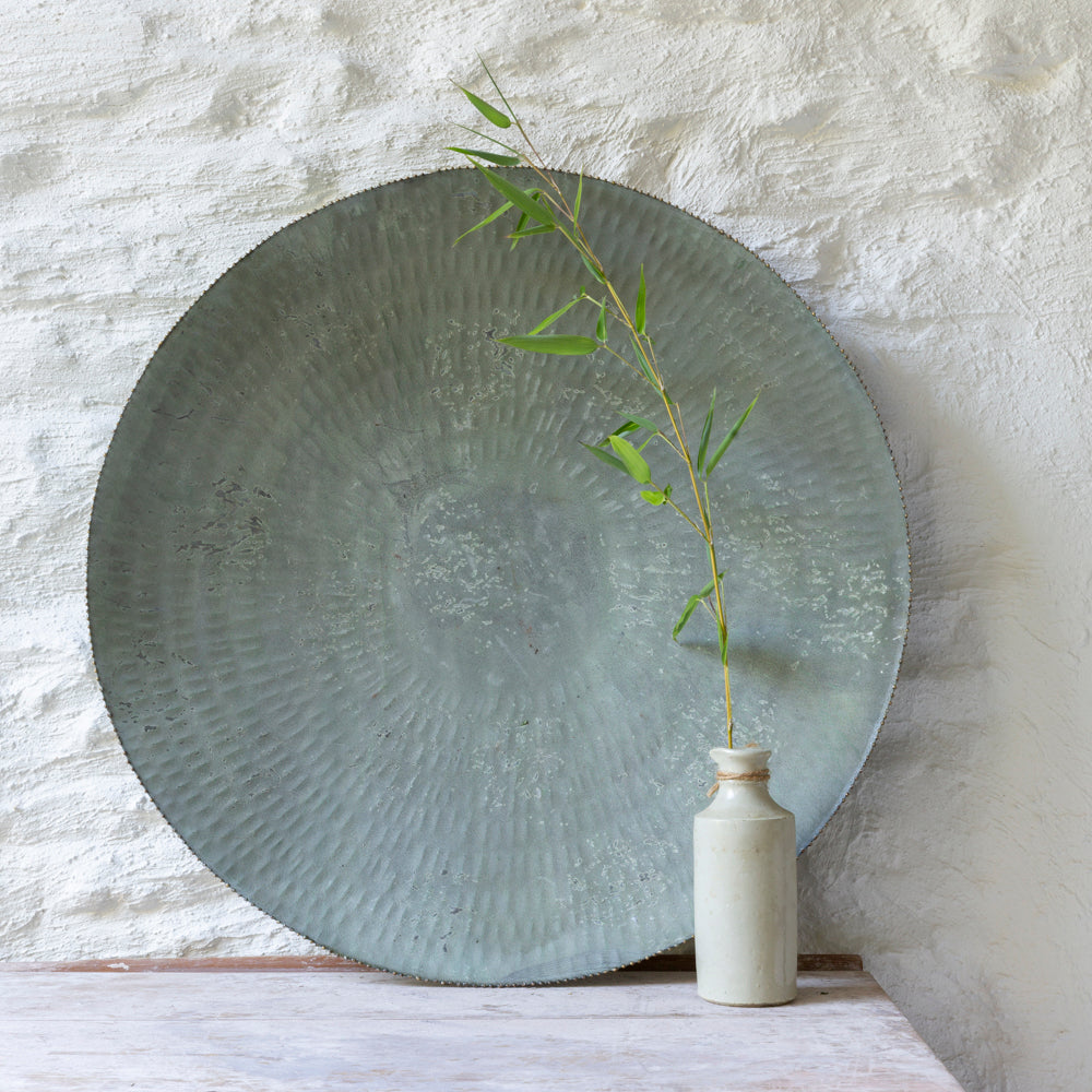 Decorative metal plate with textured surface on a wooden surface against a textured white wall.
